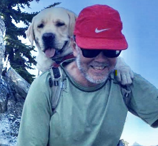 Ross smiling wearing red hat with dog on his back