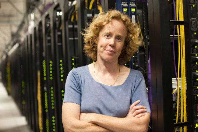 Christina Page has her arms crossed and is standing in front of a bank of servers.