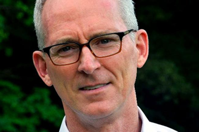 Bob Inglis is a light-skinned male with short grey hair. He smiles and wears brown-rimmed glasses and a white shirt.