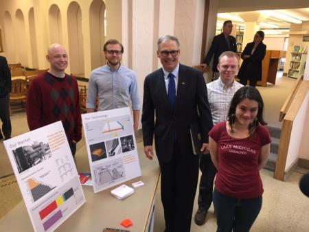 Governor Jay Inslee poses with students next to a table